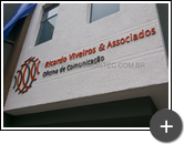 Letreiro com logotipo em formato geométrico nas cores laranja e cinza produzido em aço galvanizado para Oficina de Comunicação Ricardo Viveiros