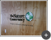 Letreiro de acrílico com pintura na cor preto fosco e logotipo com adesivo em impressão digital em formato circular representando o setor do meio ambiente da empresa - The Nature Conservancy
